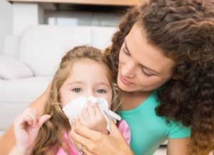 Mother helping her daughter blow her nose at home in living room